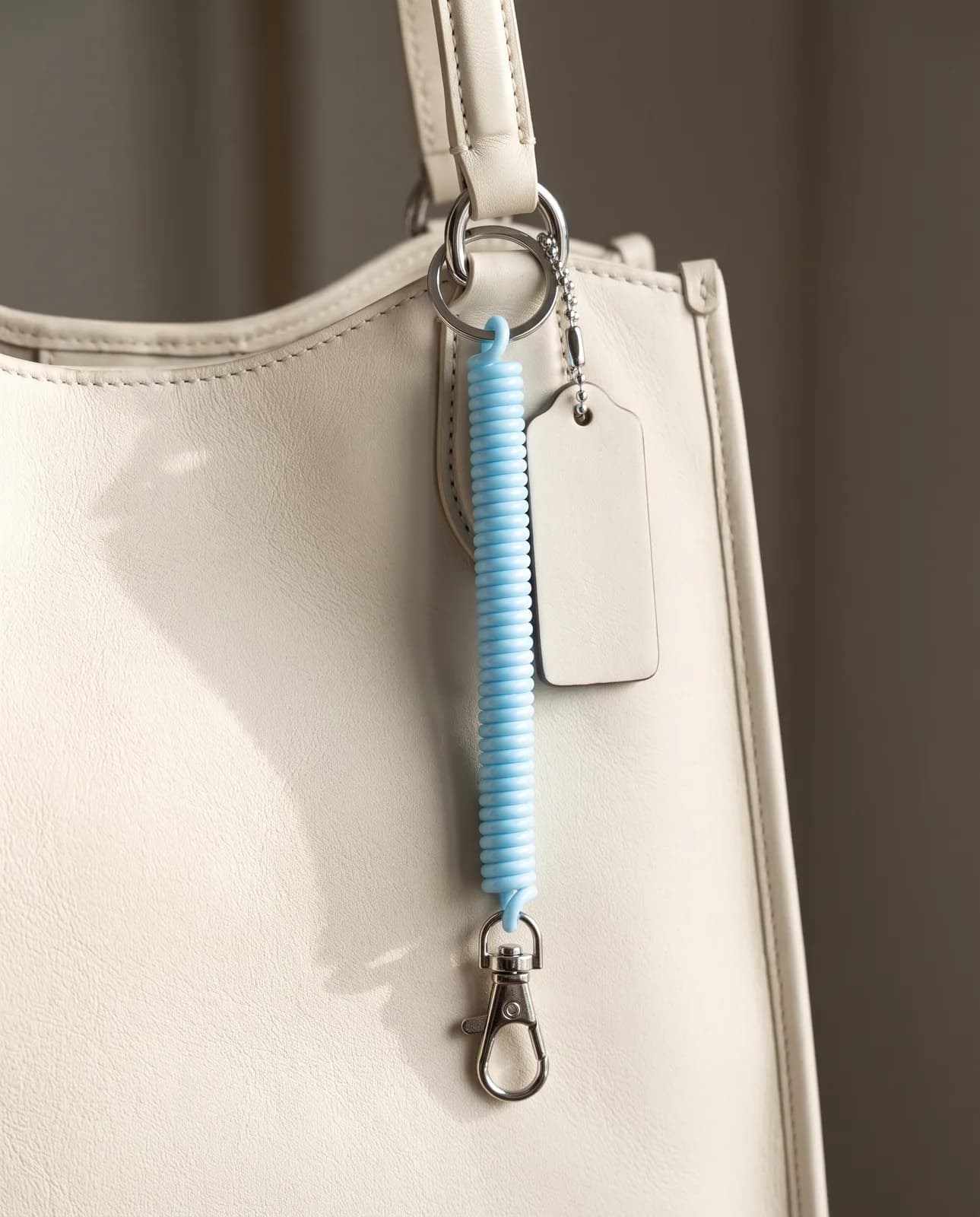 Sky blue coil keychain clipped to a cream leather handbag