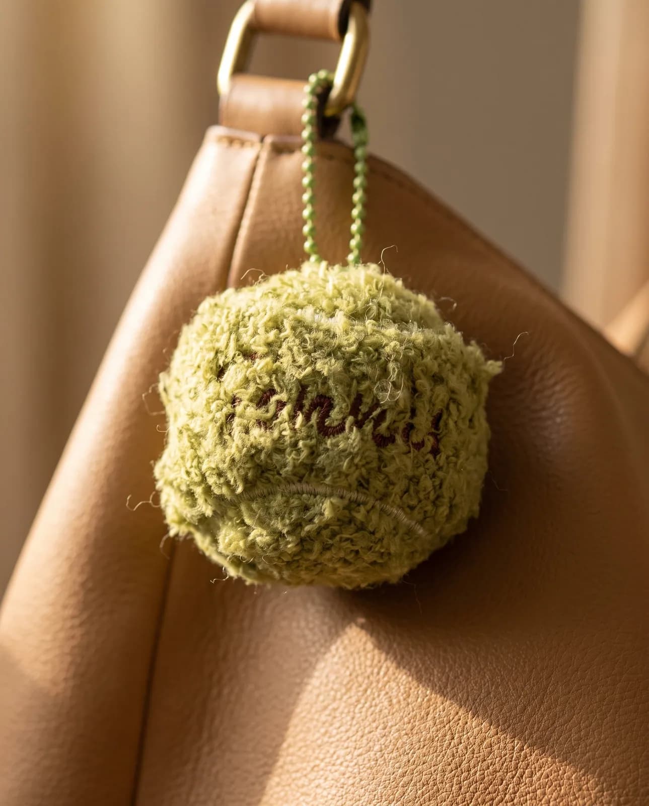 Olive bouclé ball charm on a tan leather handbag