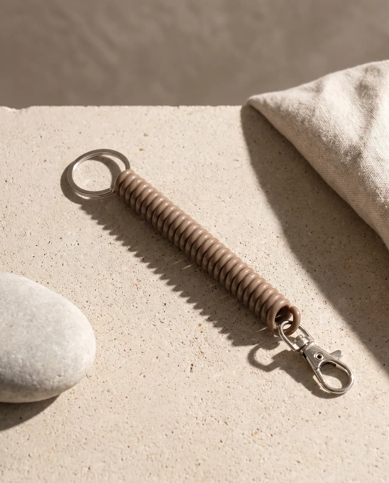 Taupe coil keychain on pale concrete in hard light