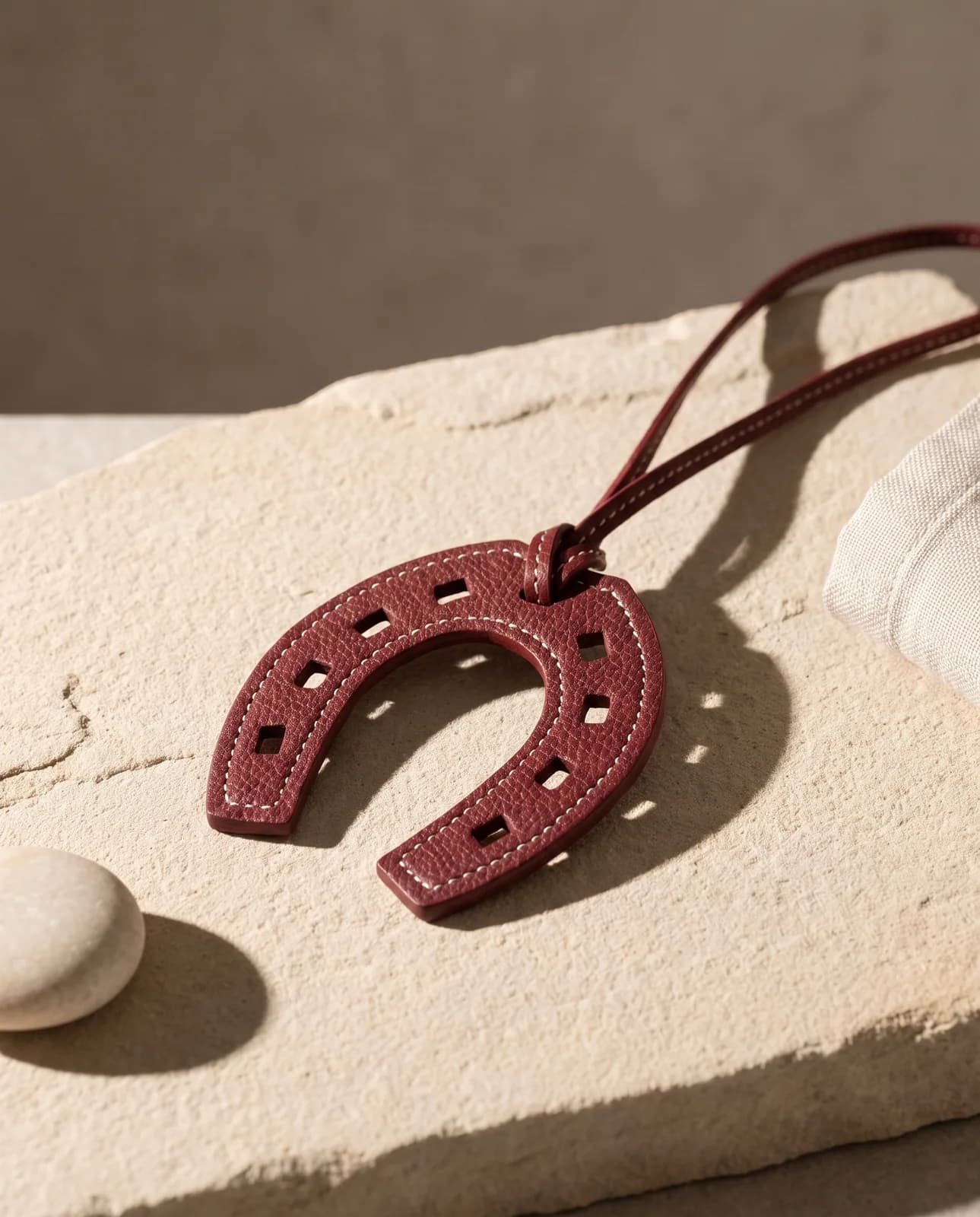 Burgundy leather horseshoe charm on sandstone in hard light