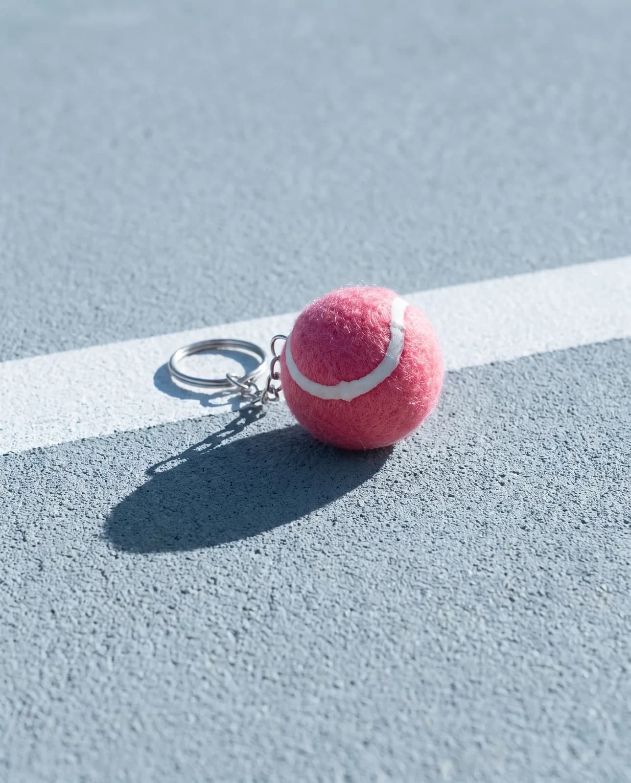 Pink tennis ball keyring on a grey-blue hard court