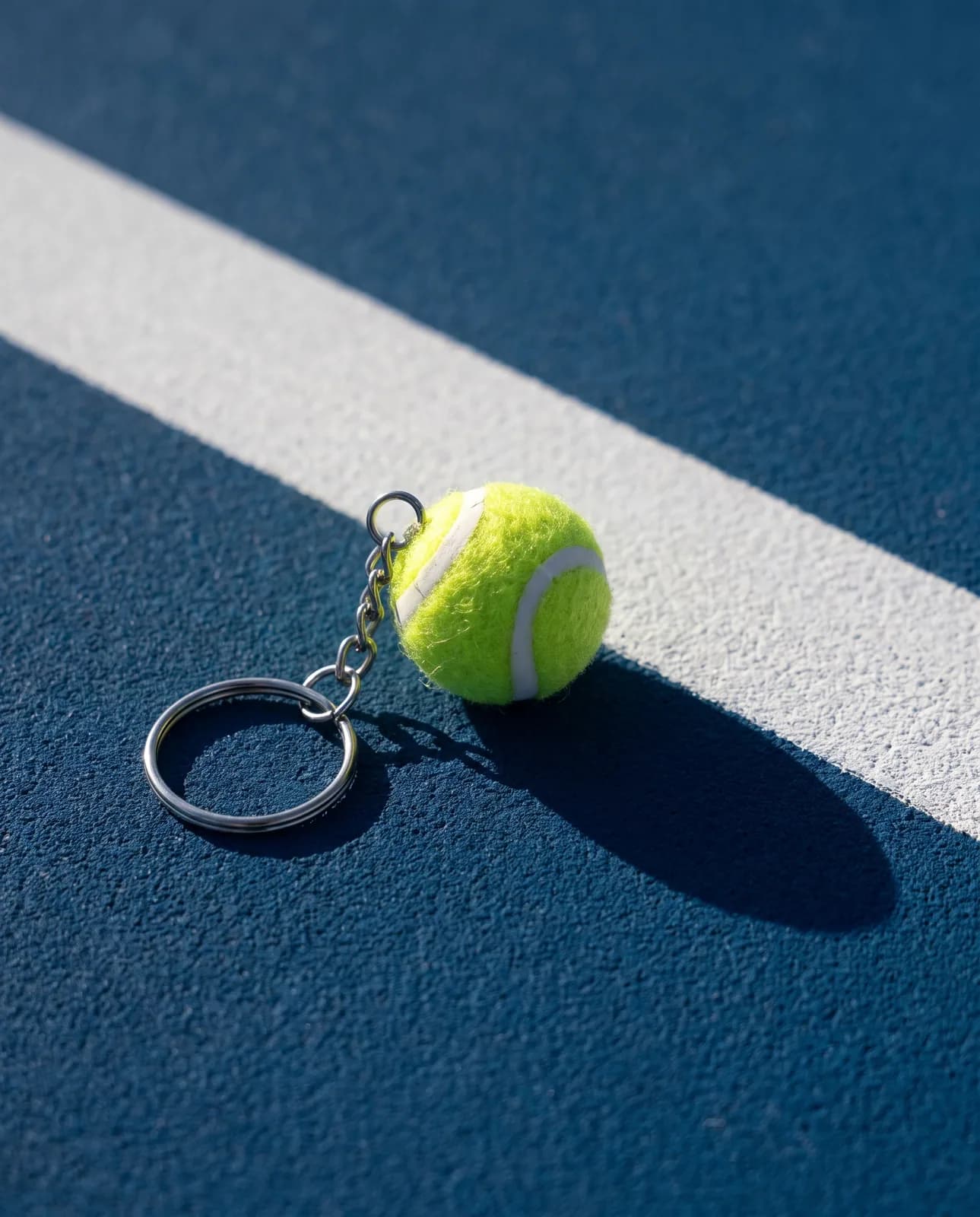 Yellow tennis ball keyring on a blue hard court